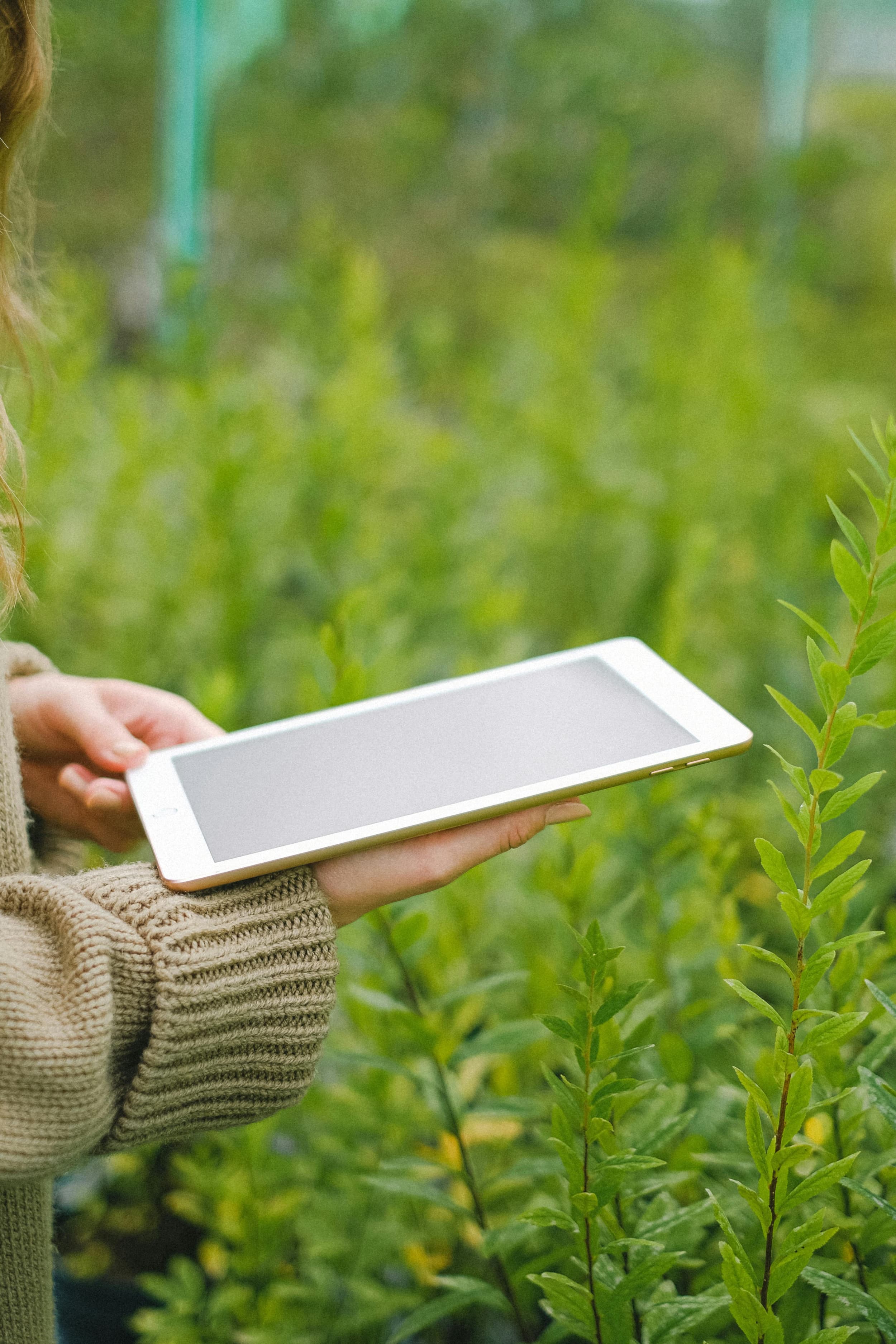 Una mujer al aire libre en un jardín, sosteniendo una tableta y disfrutando del entorno natural.